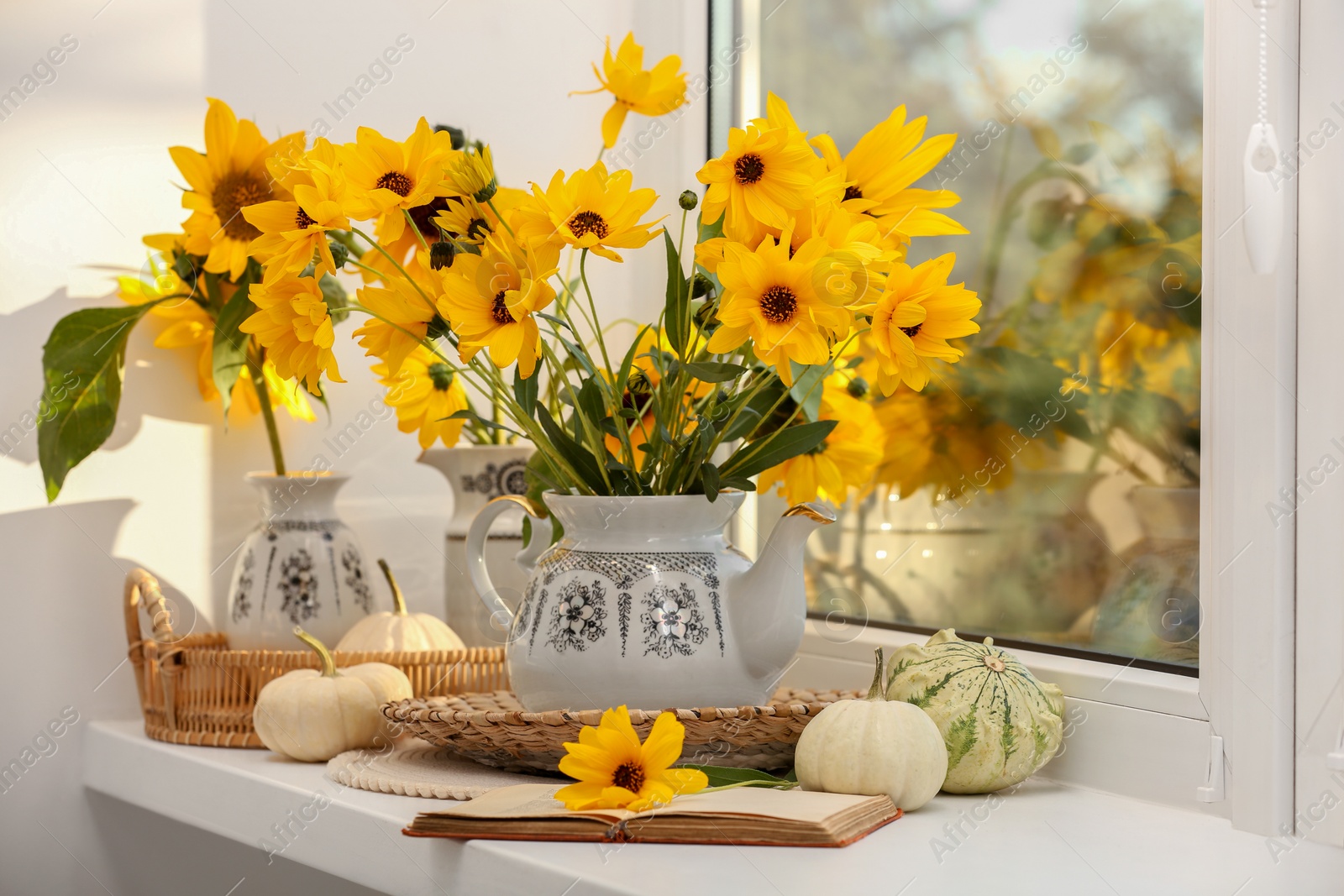 Photo of Composition with beautiful flowers, pumpkins and book on windowsill. Autumn atmosphere