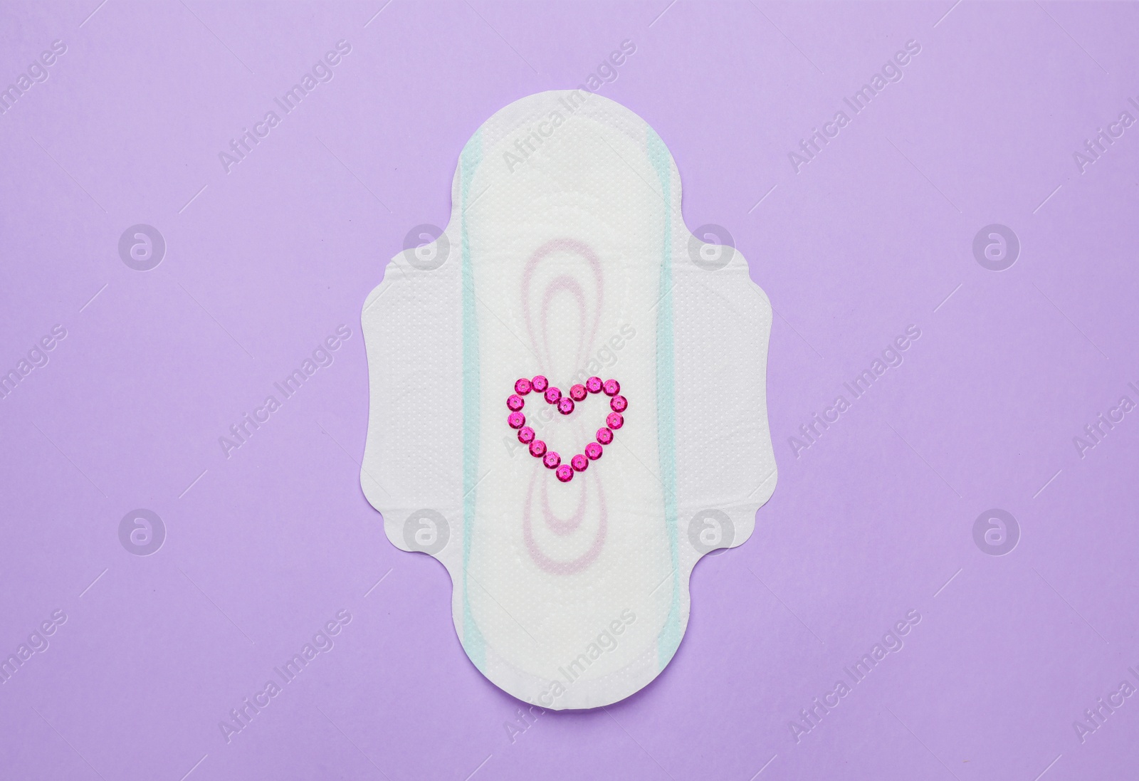 Photo of Menstrual pad with heart made of pink sequins and on violet background, top view