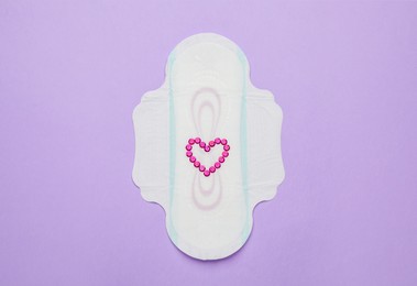 Photo of Menstrual pad with heart made of pink sequins and on violet background, top view