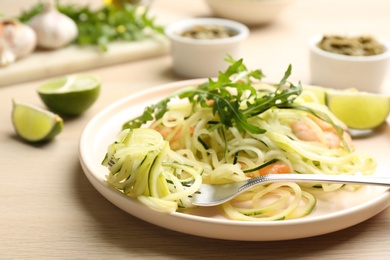 Photo of Tasty zucchini pasta with shrimps and arugula served on wooden table, closeup