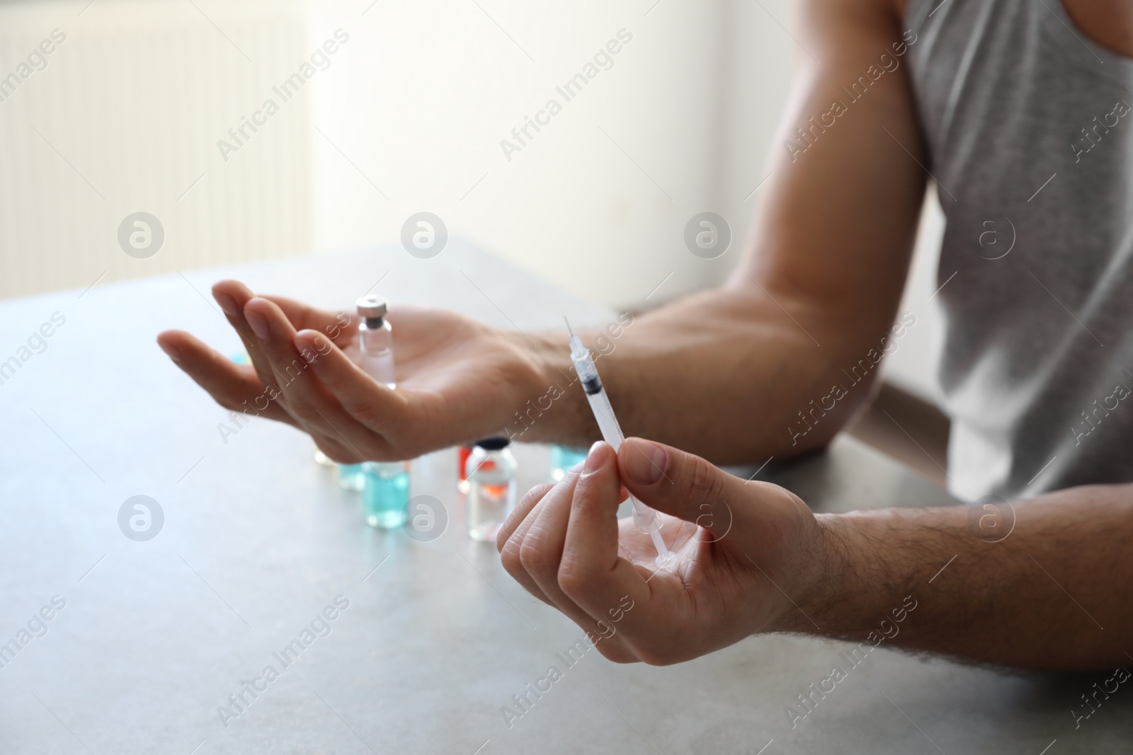 Photo of Man with syringe and vial at grey table, closeup. Doping concept