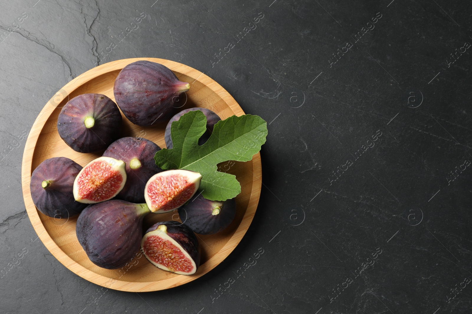 Photo of Plate with fresh ripe figs and green leaf on black table, top view. Space for text