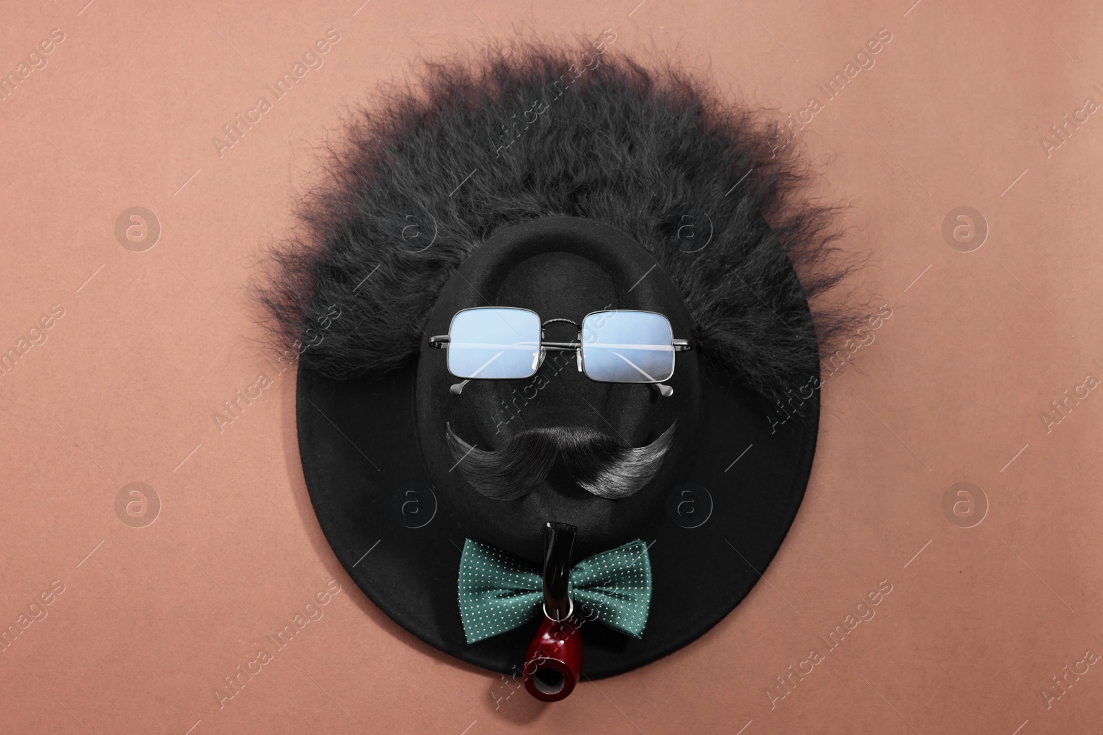 Photo of Man's face made of artificial mustache, sunglasses and hat on brown background, top view