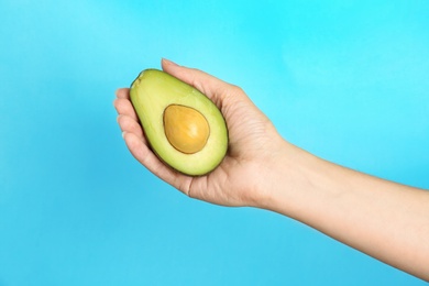 Woman holding ripe cut avocado on color background