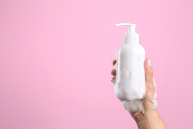 Photo of Woman with foam on hand holding bottle of skin cleanser against pink background, closeup and space for text. Cosmetic product