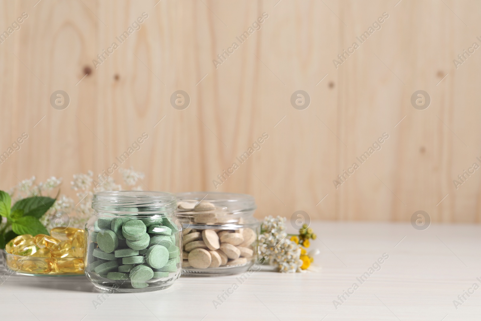 Photo of Jars with different pills on white wooden table, space for text. Dietary supplements