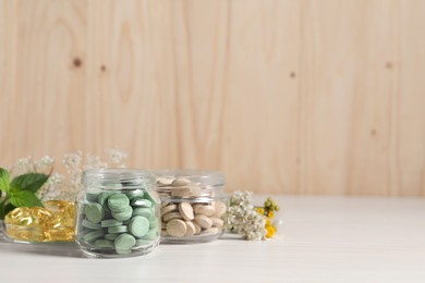 Jars with different pills on white wooden table, space for text. Dietary supplements