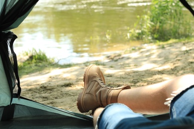 Young man resting in camping tent on riverbank, view from inside