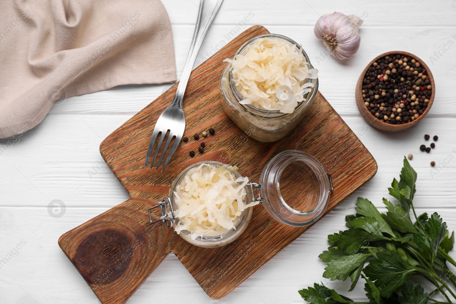 Photo of Glass jars with tasty sauerkraut and ingredients on white wooden table, flat lay