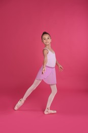 Photo of Little ballerina practicing dance moves on pink background