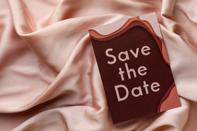 Photo of Beautiful wedding invitation card with Save the Date phrase on pink fabric, top view. Space for text
