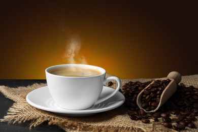 Cup of hot aromatic coffee and roasted beans on black table against brown background