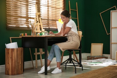 Photo of Young woman drawing with watercolors at table indoors