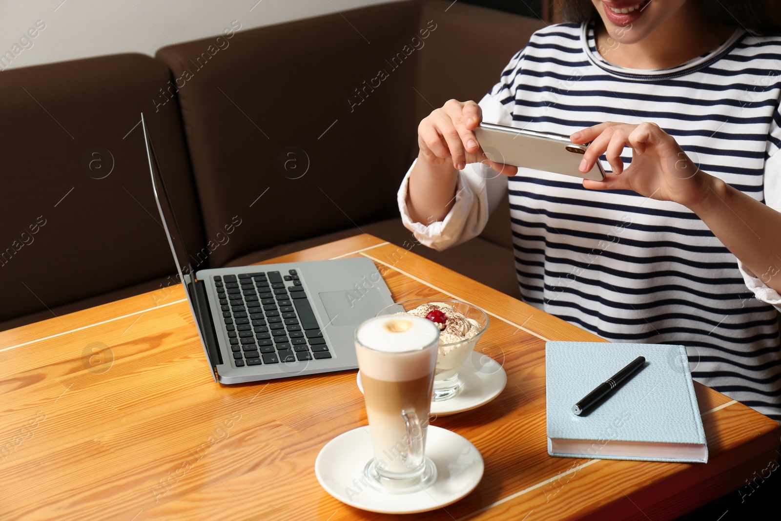 Photo of Young blogger taking picture of dessert and latte at table in cafe, closeup