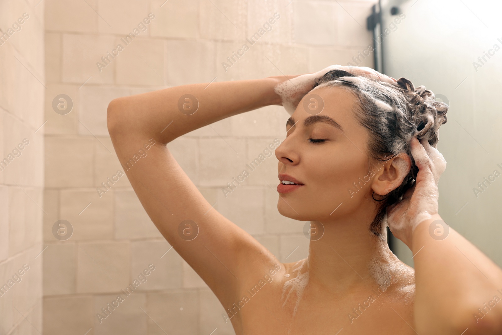 Photo of Young woman washing hair while taking shower at home