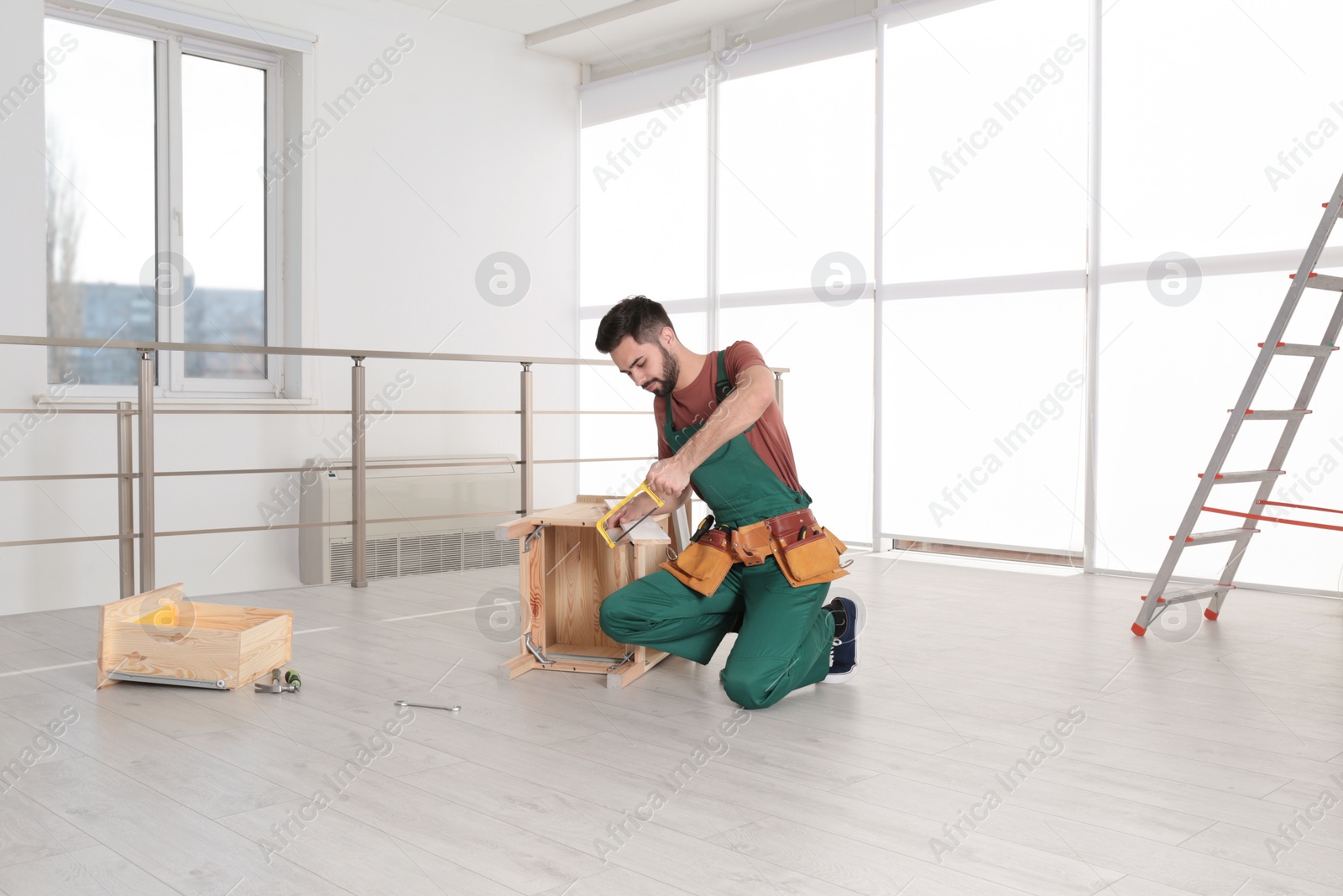 Photo of Carpenter in uniform making furniture indoors. Professional construction tools