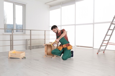 Carpenter in uniform making furniture indoors. Professional construction tools