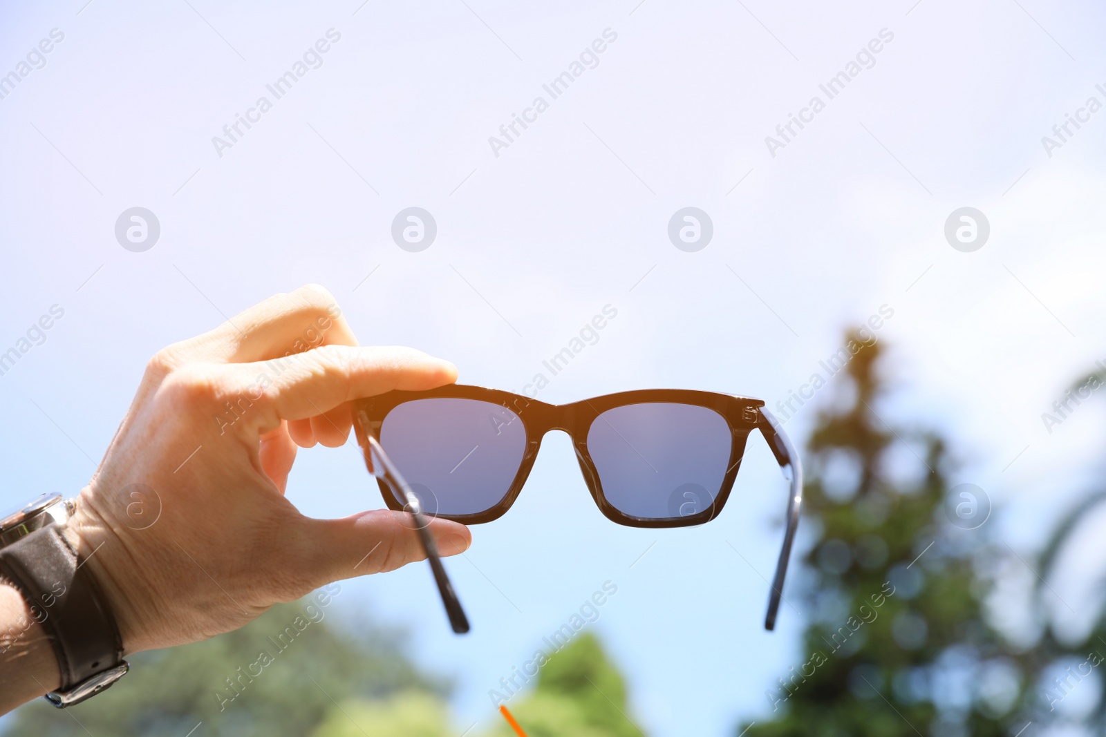 Photo of Mature man holding stylish sunglasses outdoors on sunny day, closeup