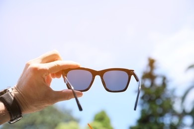 Mature man holding stylish sunglasses outdoors on sunny day, closeup