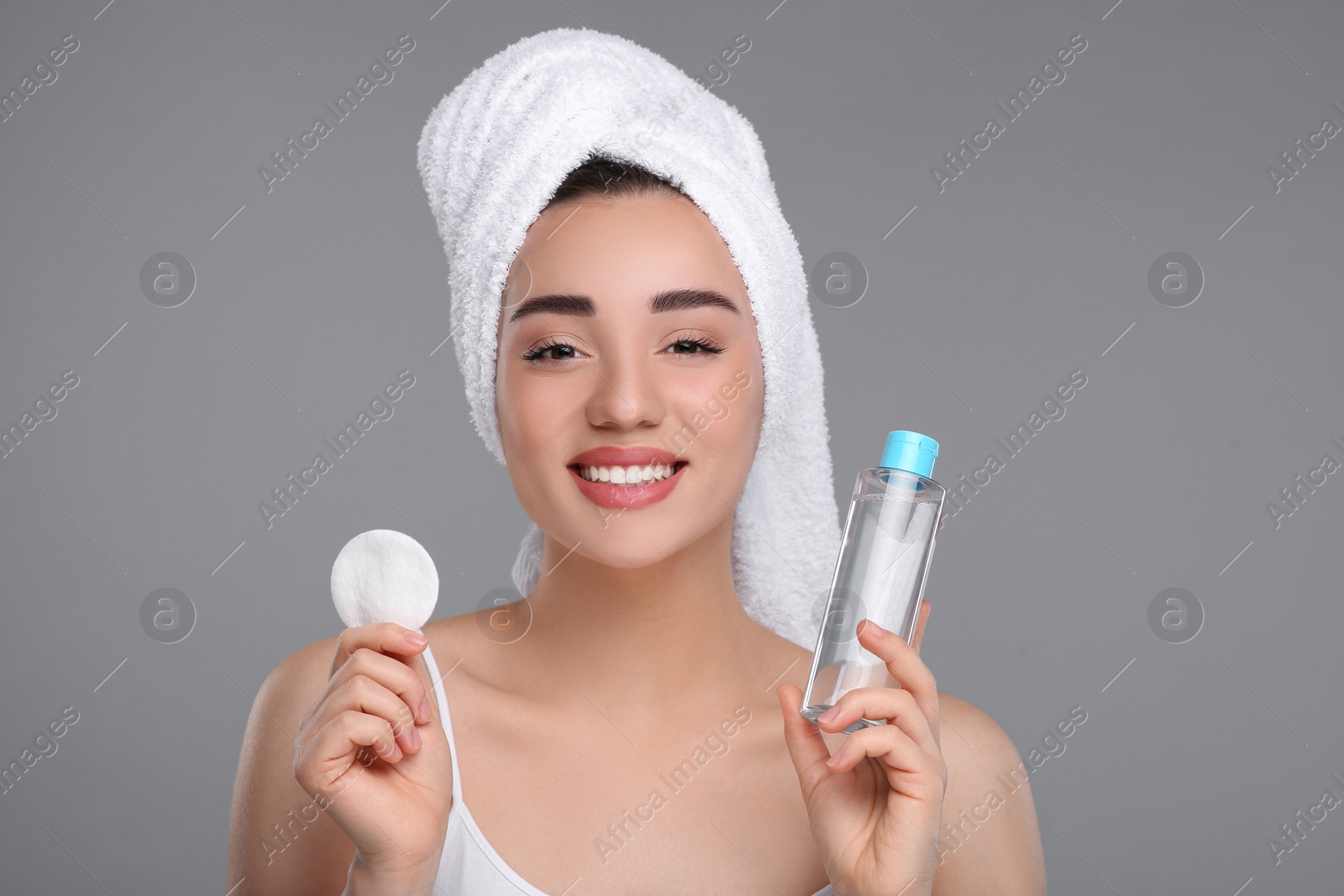 Photo of Beautiful woman in terry towel with makeup remover and cotton pad on gray background