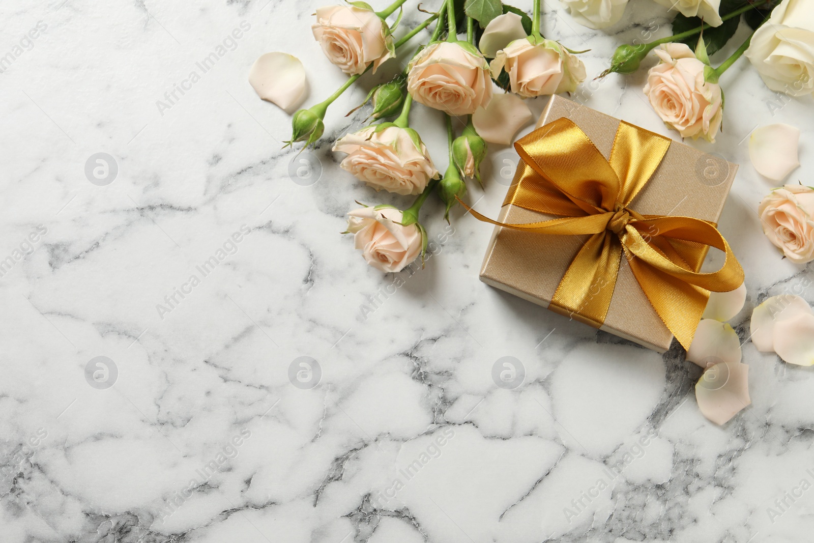 Photo of Golden gift box and beautiful roses on white marble background, flat lay. Space for text