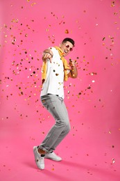 Photo of Happy man dancing and confetti on pink background