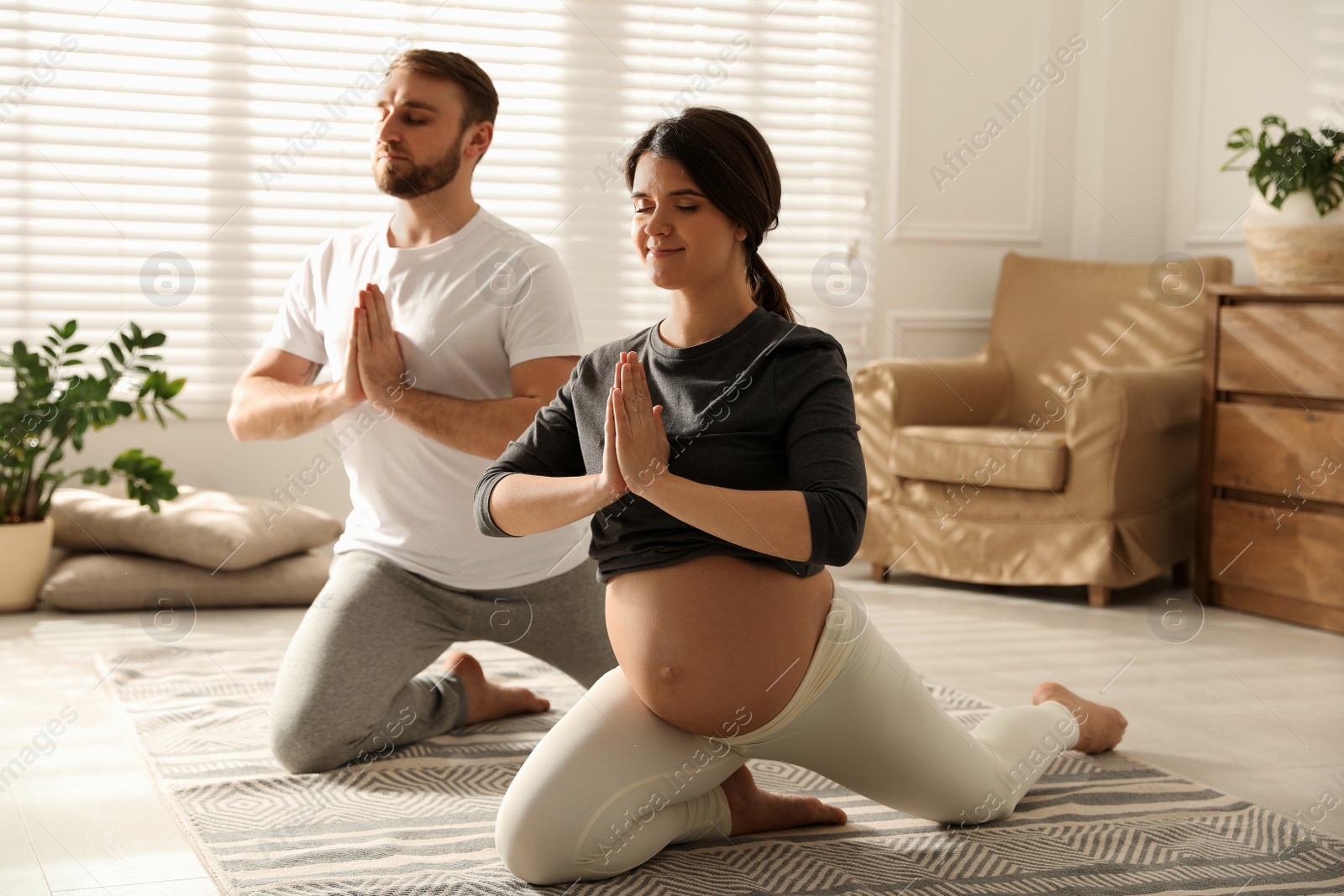Photo of Young pregnant woman with her husband practicing yoga at home