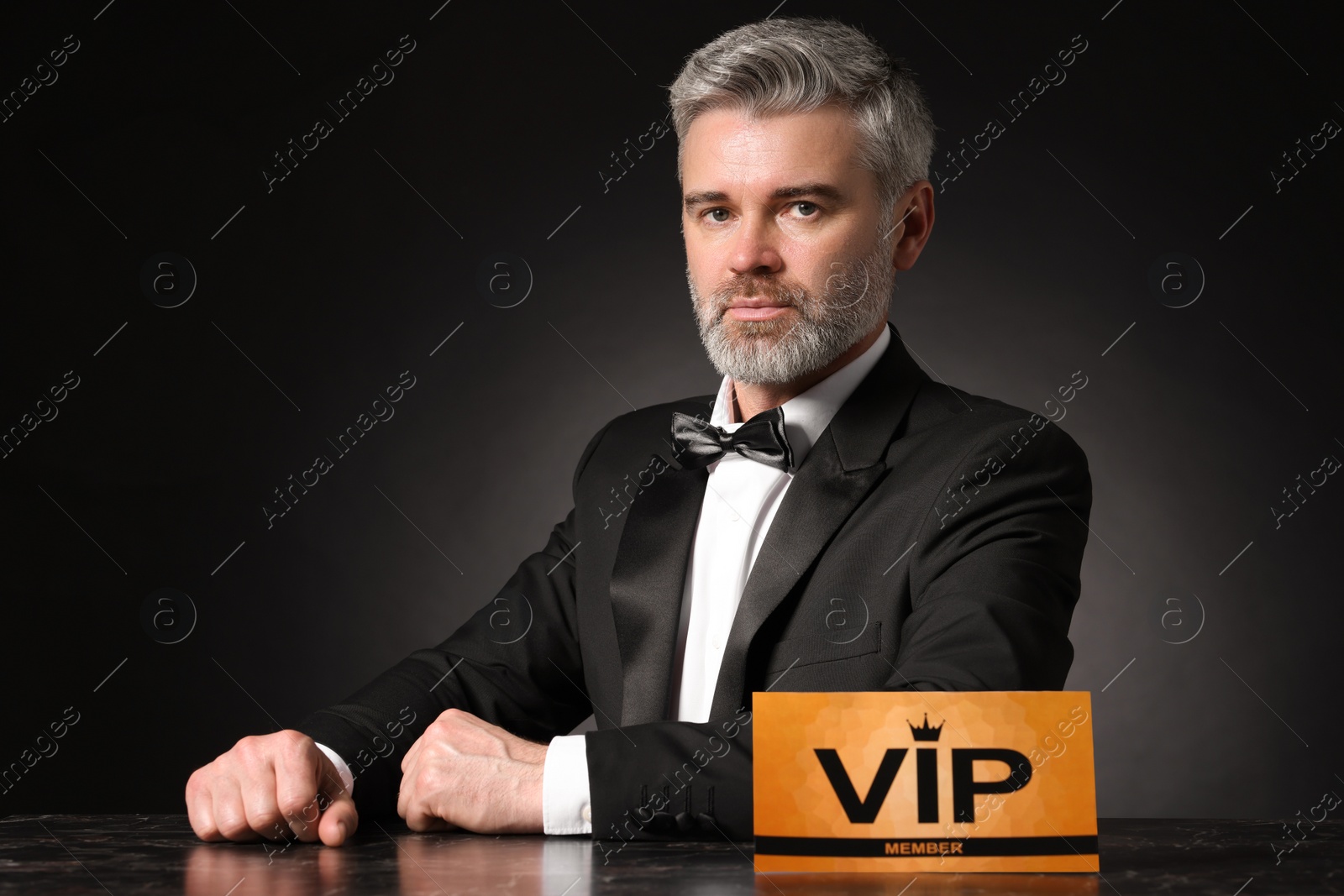 Photo of Handsome man sitting at table with VIP sign on black background
