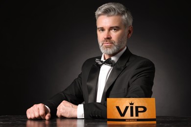 Handsome man sitting at table with VIP sign on black background