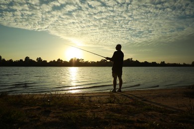 Photo of Fisherman with rod fishing at riverside at sunset