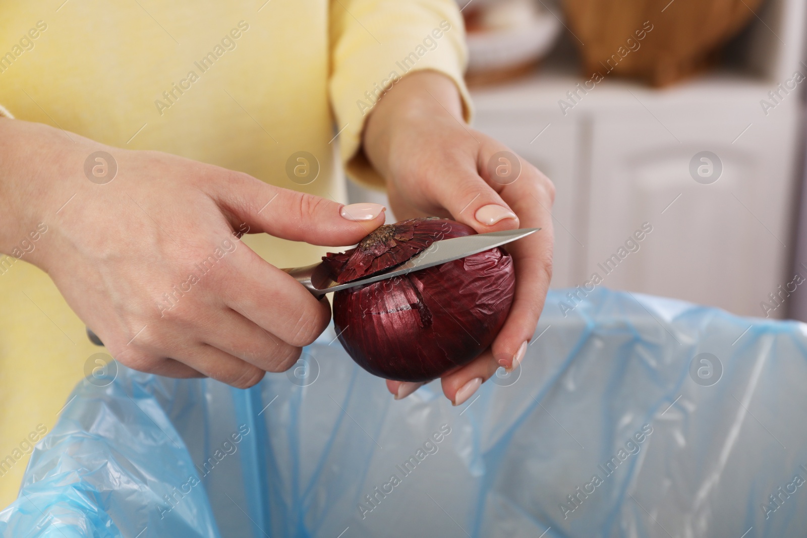 Photo of Woman peeling fresh onion with knife above garbage bin indoors, closeup