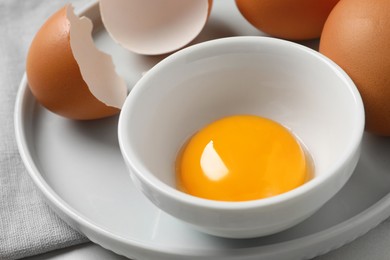 Photo of Chicken eggs and bowl with raw yolk on table, closeup