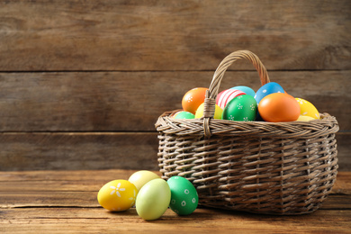 Photo of Colorful Easter eggs in basket on wooden background. Space for text