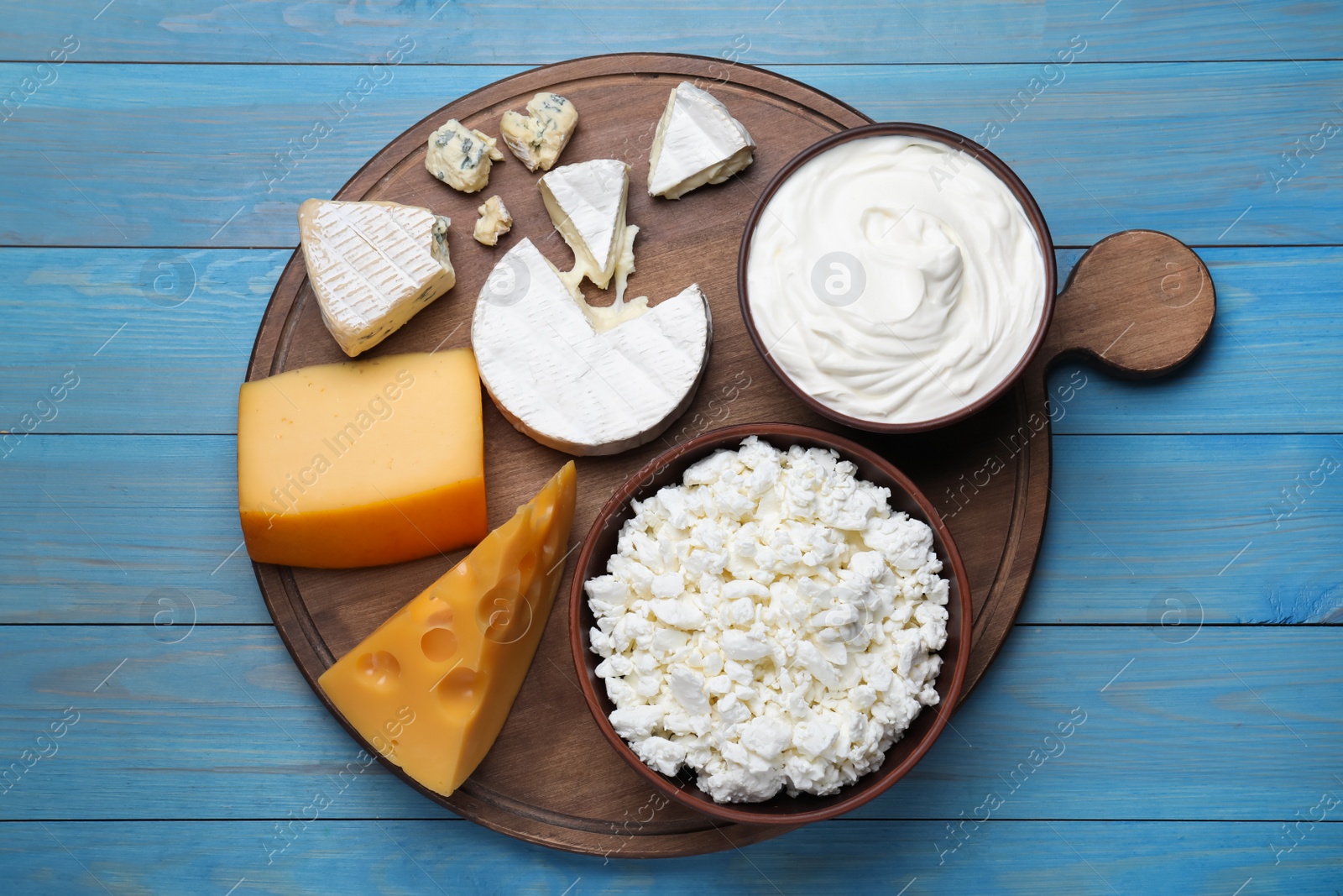 Photo of Clay dishware with fresh dairy products on blue wooden table, top view