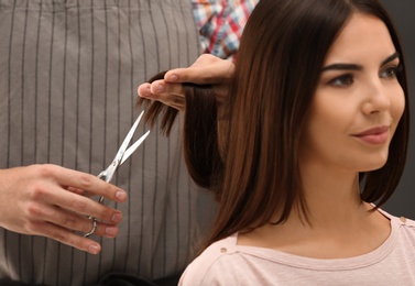 Photo of Barber making stylish haircut with professional scissors in beauty salon