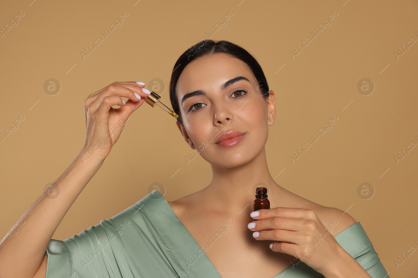 Photo of Young woman applying essential oil onto face against beige background