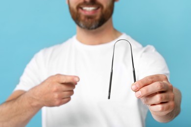 Man showing tongue cleaner on light blue background, closeup