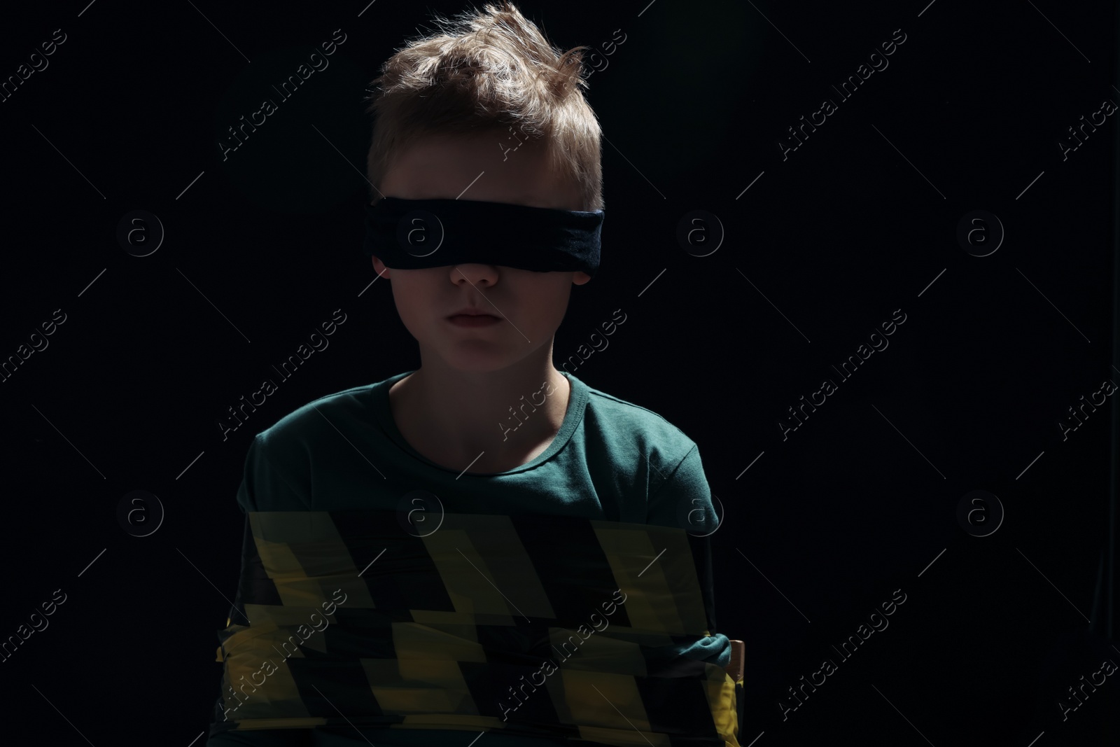 Photo of Blindfolded little boy tied up and taken hostage against dark background