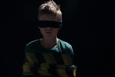 Blindfolded little boy tied up and taken hostage against dark background