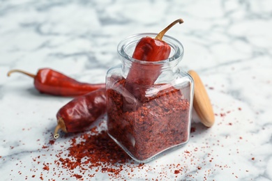 Photo of Jar with crushed chili pepper and pods on light background