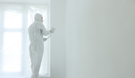 Photo of Decorator painting wall with spray indoors, space for text