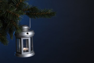 Christmas lantern with burning candle on fir tree against blue background, closeup. Space for text