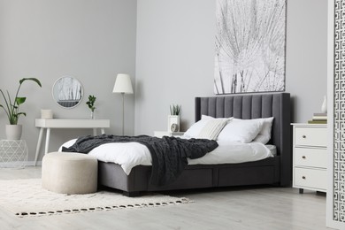 Stylish bedroom interior with large comfortable bed, chest of drawers and dressing table