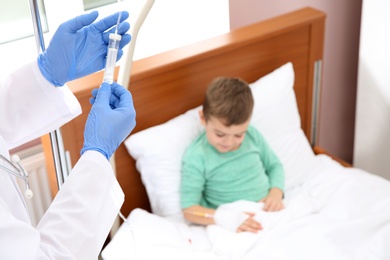 Photo of Doctor adjusting intravenous drip for little child in hospital, closeup