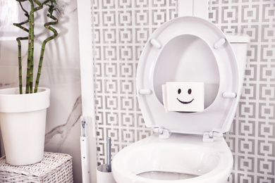 Roll of paper with funny face on toilet seat in bathroom