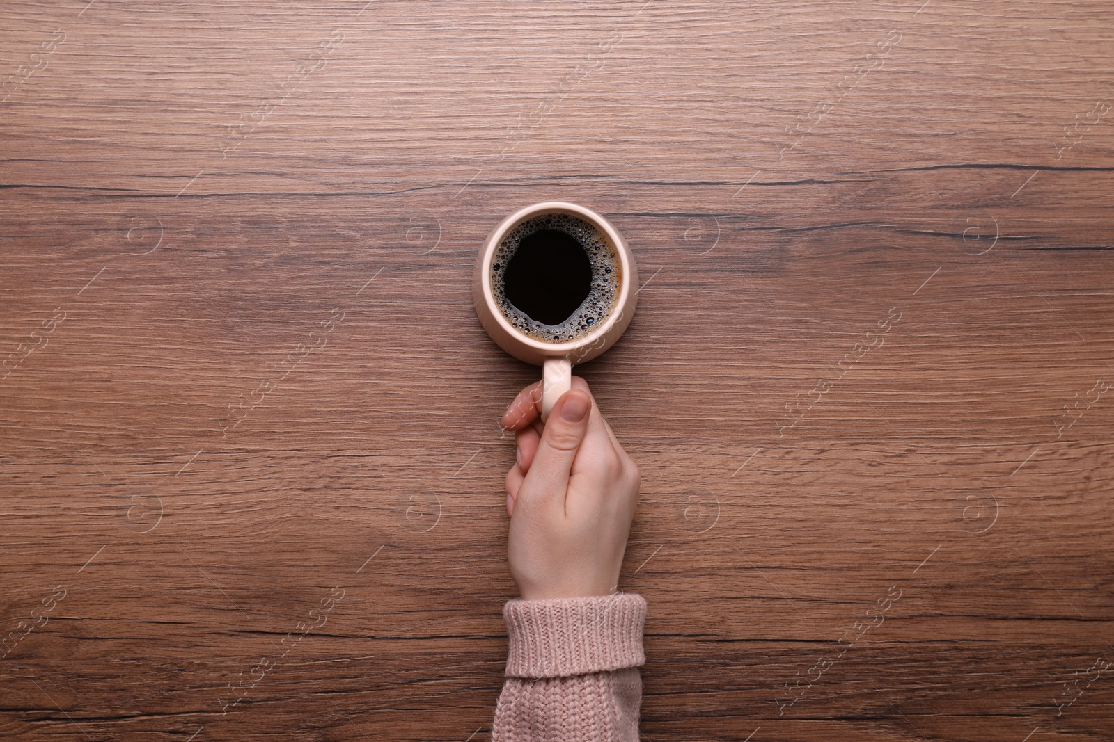 Photo of Woman with cup of coffee at wooden table, top view