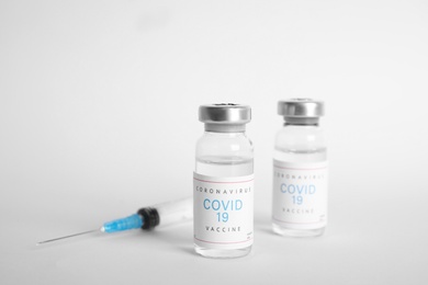 Vials with coronavirus vaccine and syringe on white background