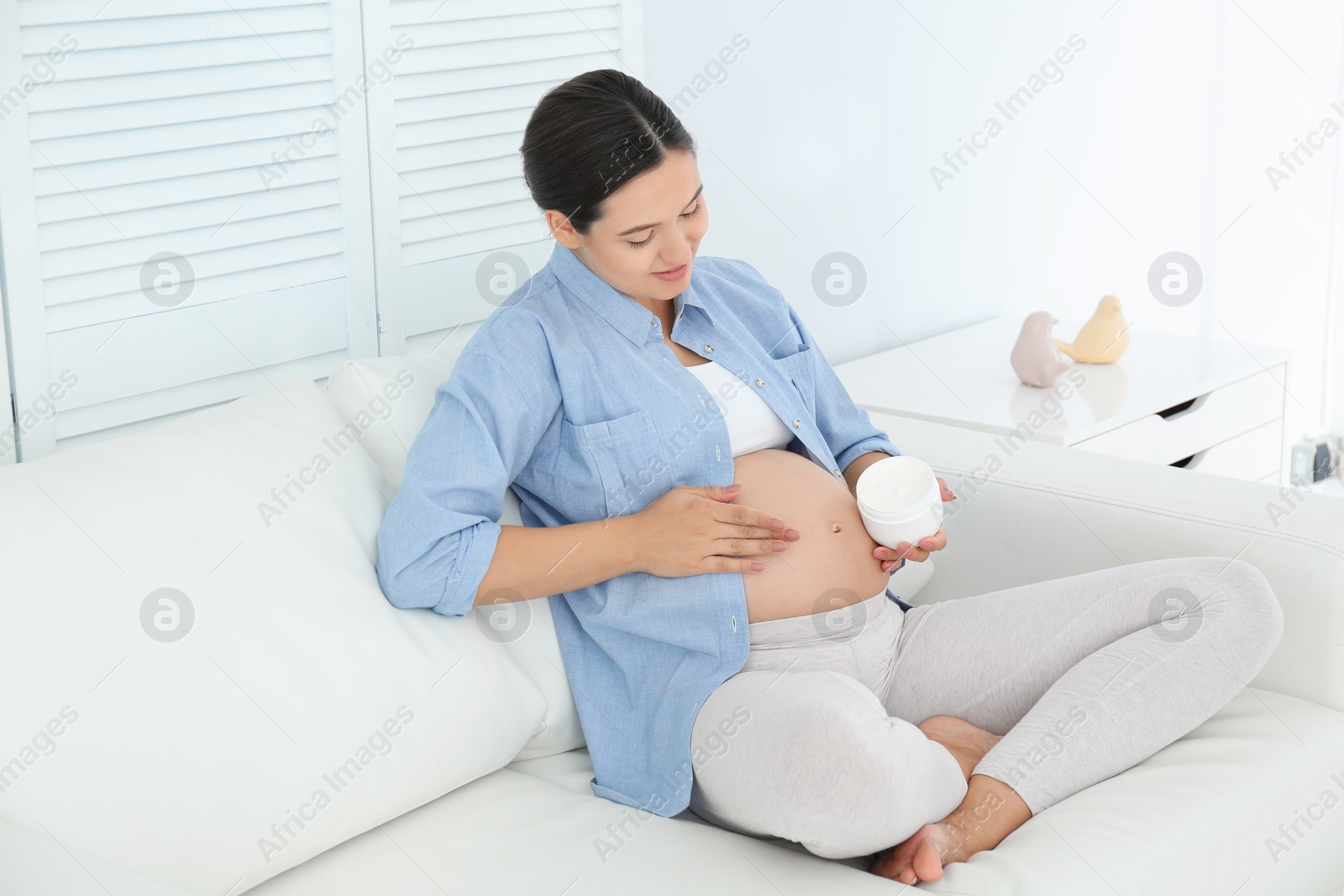 Photo of Pregnant woman applying body cream on belly at home