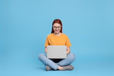 Photo of Smiling young woman working with laptop on light blue background