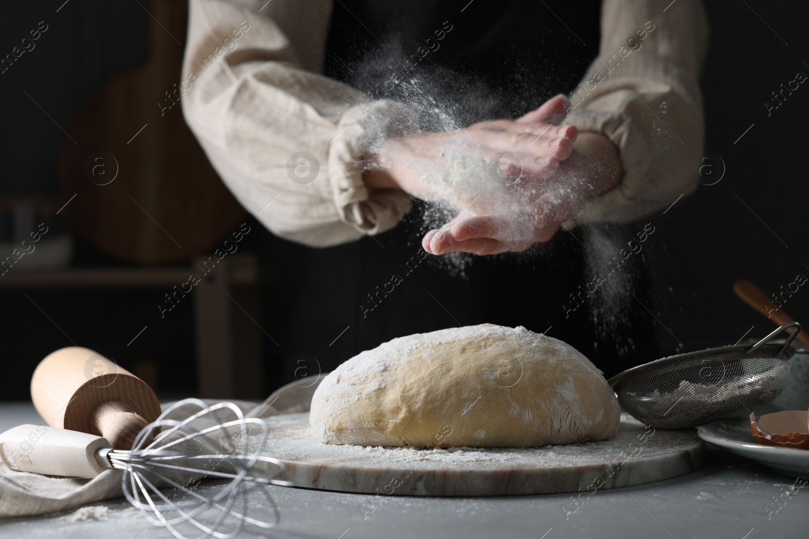 Photo of Making dough. Woman adding flour at grey table, closeup